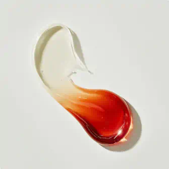 Swatch of cream blending into a rich red serum on a smooth surface