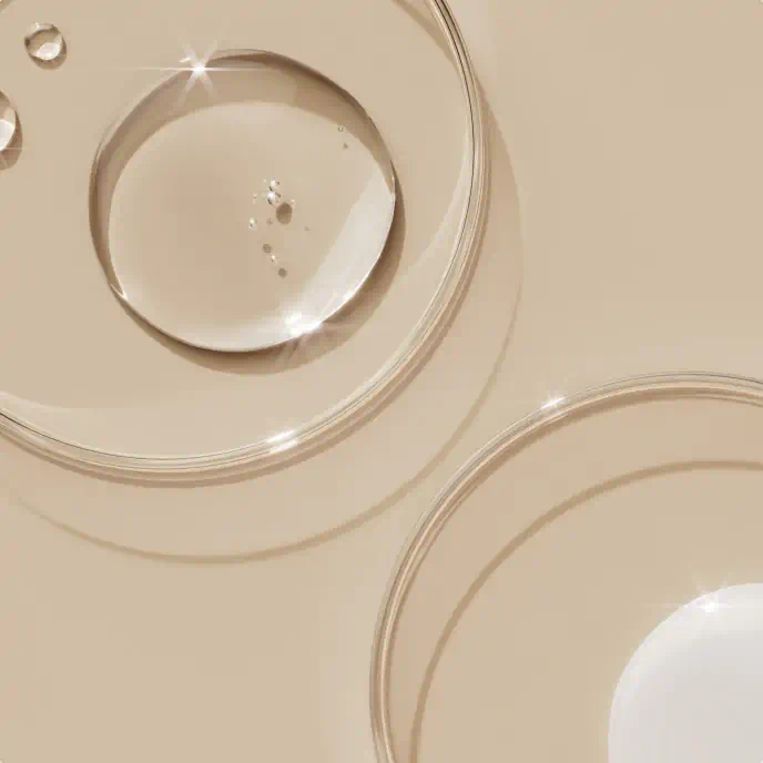 Clear skincare serum droplets in glass petri dishes on a beige background